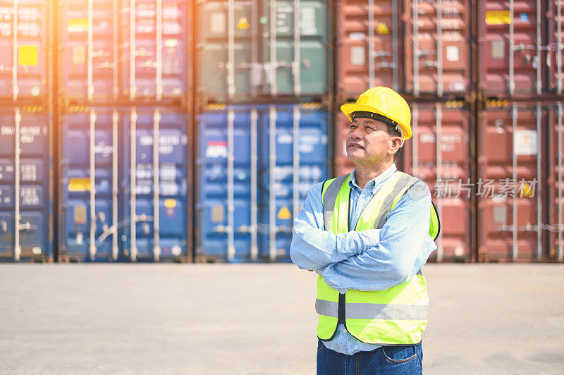 Portrait of Logistic engineer worker man standing in shipping container yard and crossed arms. Confident engineering work at container cargo site and checking industrial container cargo freight ship